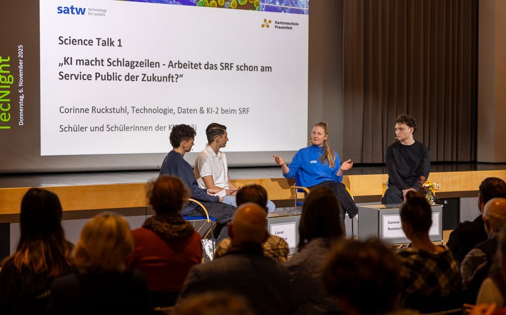 Podiumsdiskussion mit drei Teilnehmer:innen und einer Moderatorin auf der Bühne. Davor sitzt das Publikum.