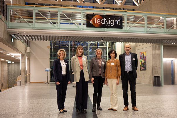 Fünf Personen stehen in einem modernen Gebäude unter einem TecNight Schild.