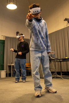 Junge mit einem VR Headset greift nach etwas in der Luft. Im Hintergrund ist ein weiterer Junge mit Headset.